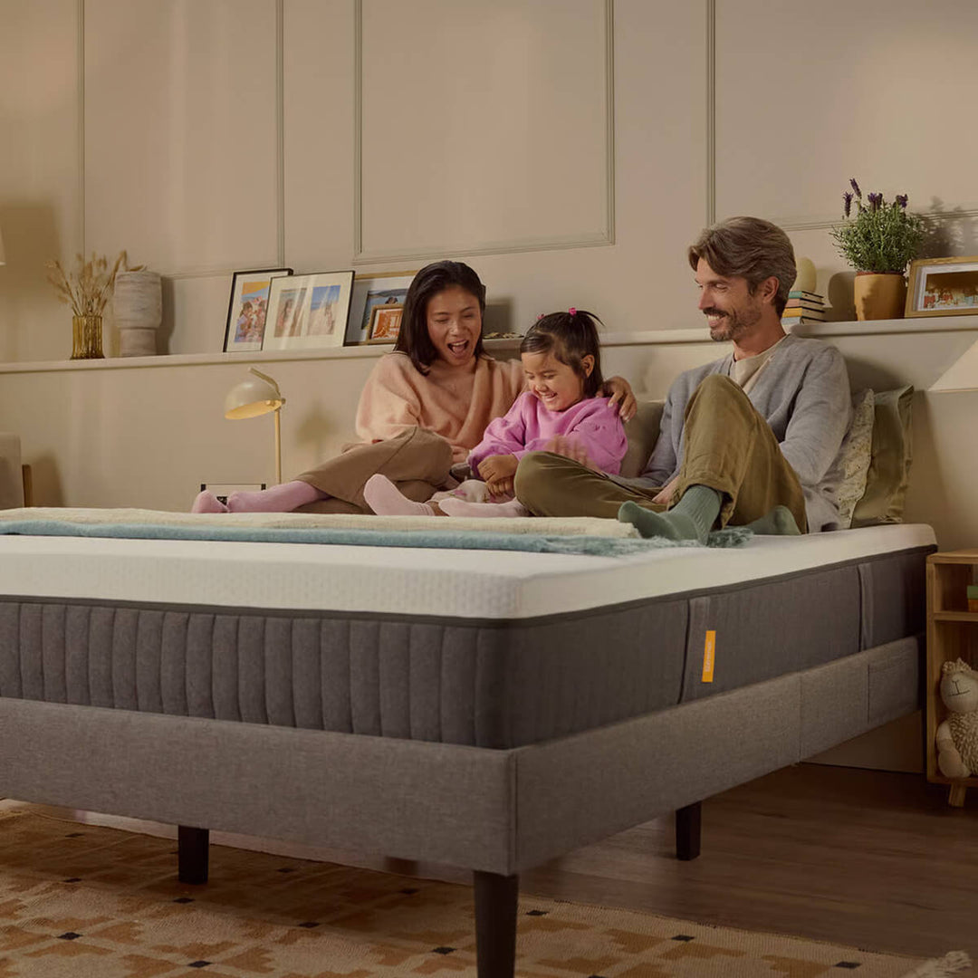 Família sentada em colchão hibrido, numa cama.
