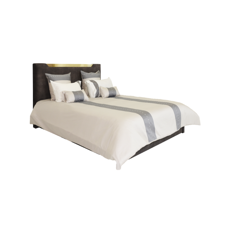 Cama de casal com cabeceira escura e detalhe dourado, roupa de cama creme com edredão e almofadas de riscas cinzentas e pontos brancos.
