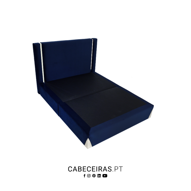 Base de cama divã azul-marinho com cabeceira estofada e detalhes prateados nas laterais e pés.