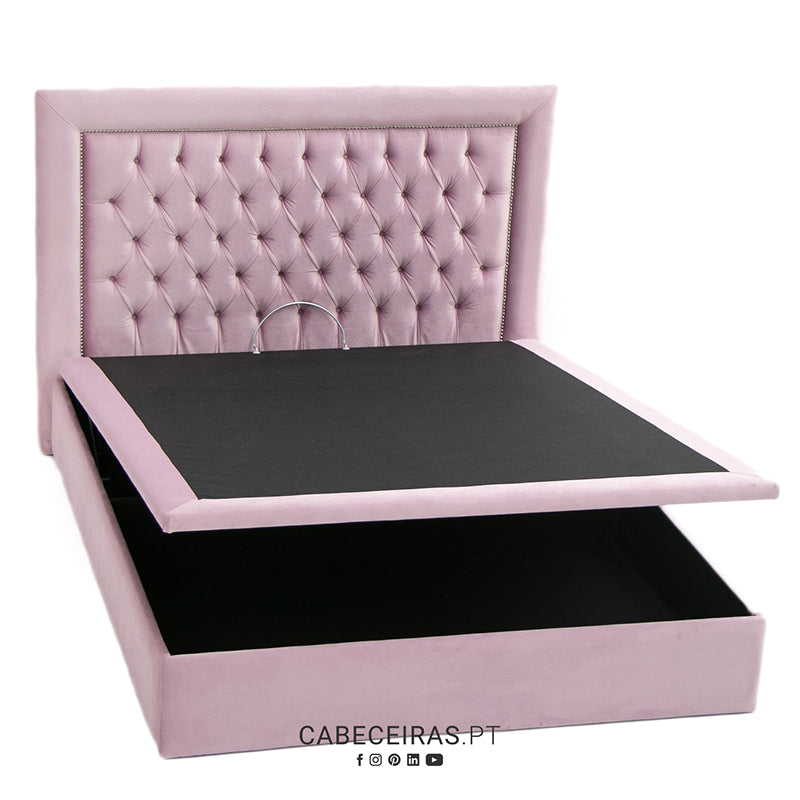 Cama divã rosa claro em veludo com cabeceira capitonê e base de arrumação aberta, mostrando o interior. Texto: CABECEIRAS.PT.