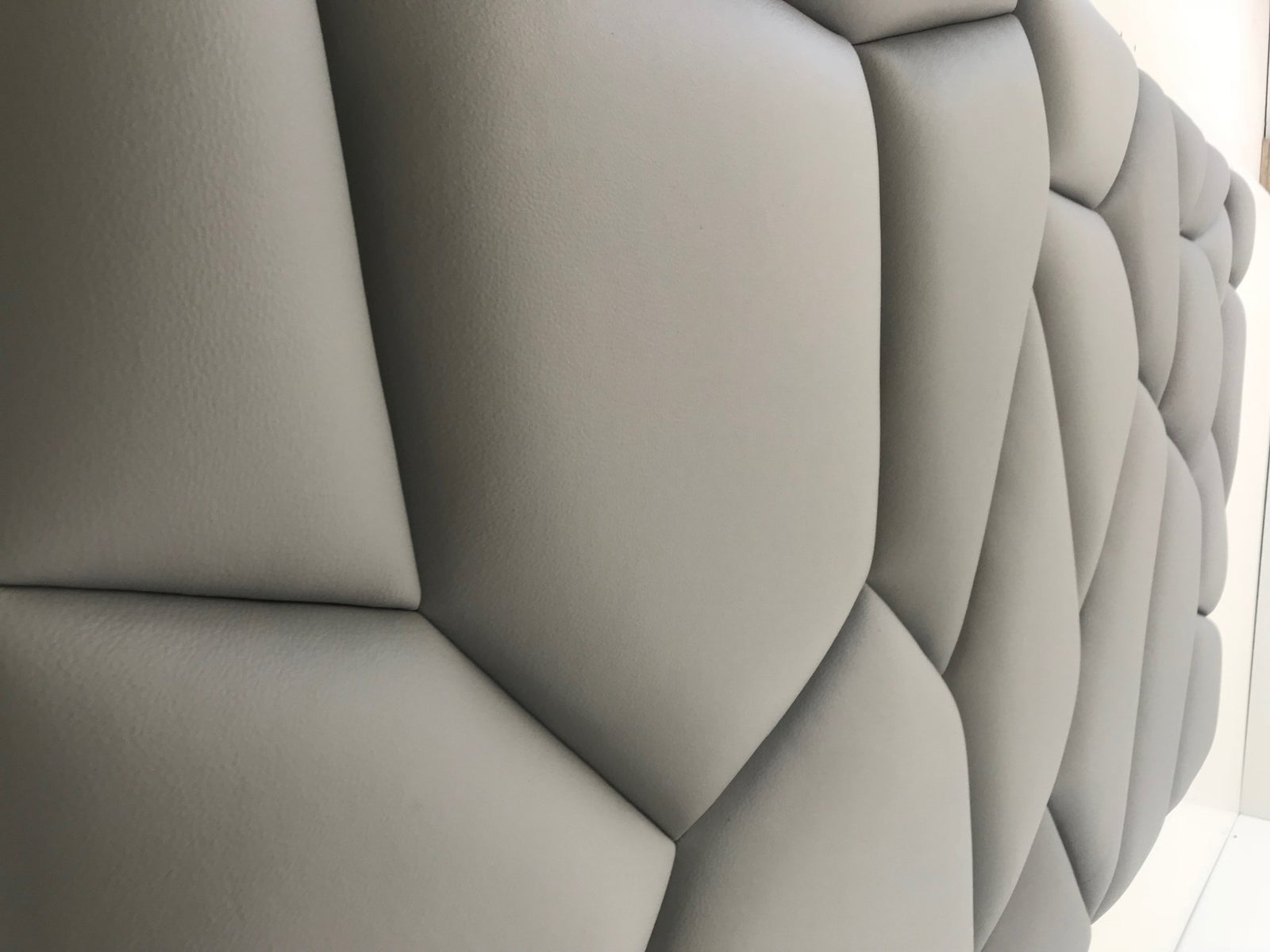 Pormenor de painel de parede estofado em cinzento claro, com design geométrico almofadado e textura em 3D.