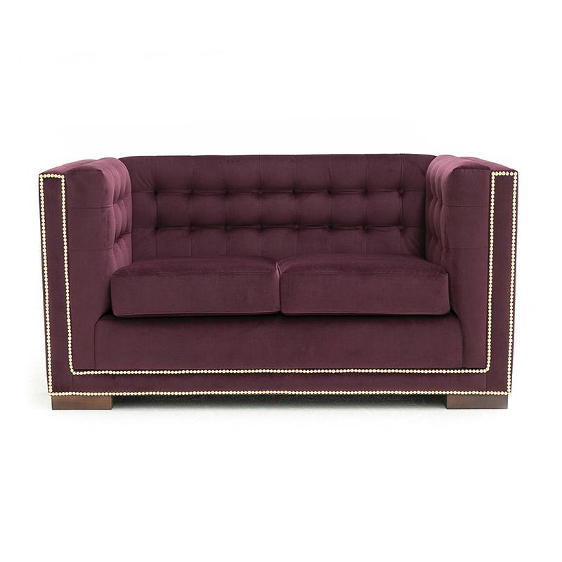 Sofá de dois lugares em veludo roxo escuro, com encosto capitonê e tachas douradas nas bordas.