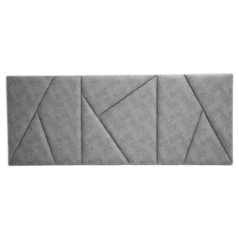 Painel estofado cinzento com padrão geométrico de costuras que criam formas triangulares e quadriláteros.